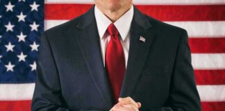 Man in suit with red tie standing before American flag