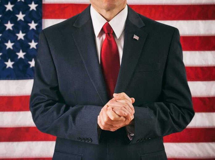 Man in suit with red tie standing before American flag