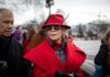 Jane Fonda in a red coat and hat with Walter Jones beside her outdoors