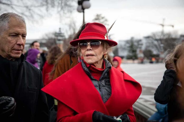 Jane Fonda in a red coat and hat with Walter Jones beside her outdoors