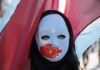 Nobel Uproar: UN Star Linked To Uyghur Betrayals Person wearing a blue protest mask with flags