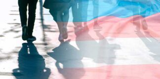trans pride flag overlaying silhouettes of people walking on a city street