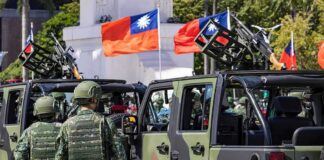Soldiers beside camouflaged military vehicles with mounted guns and flags