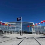 NATO headquarters with member flags in front under a clear blue sky