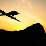 Drone silhouette flying over mountains at sunset