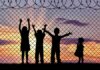 Children silhouetted against a chain-link fence at sunset