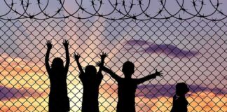 Children silhouetted against a chain-link fence at sunset