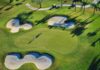 Golfers on a green surrounded by sand bunkers