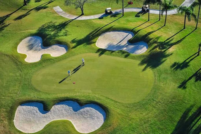 Golfers on a green surrounded by sand bunkers